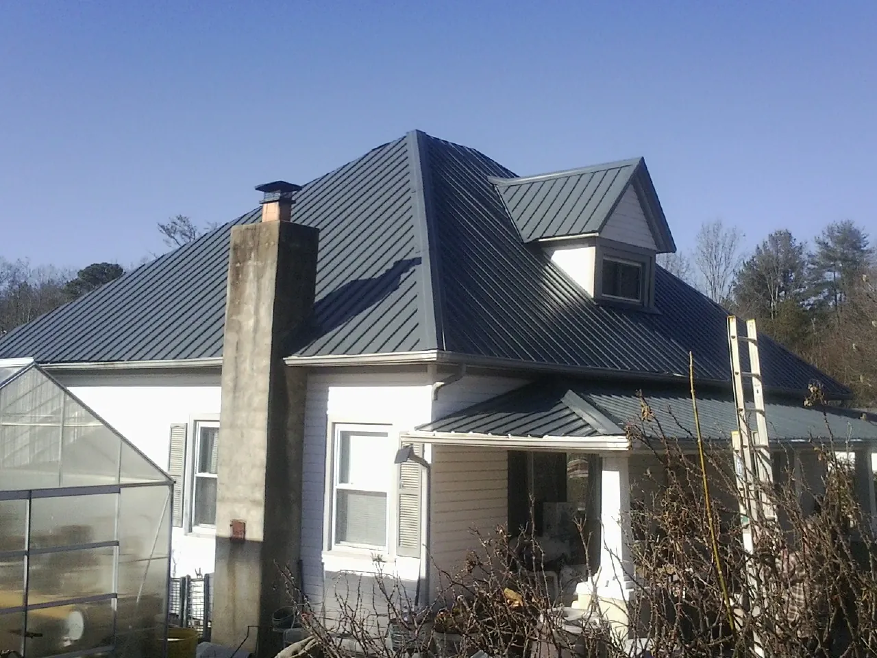 Dark blue standing seam metal roof on a white farmhouse with dormer — Slate & Tile Roof Repair by Roofing Brothers in Mineral Point