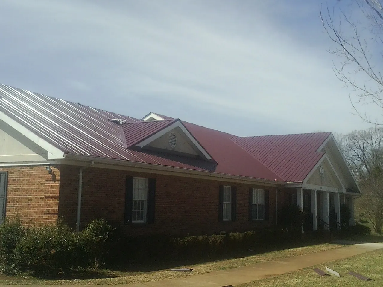 Red metal roof with gabled entries on a long brick building, from a Hail Damage Roof Repair job in Mineral Point