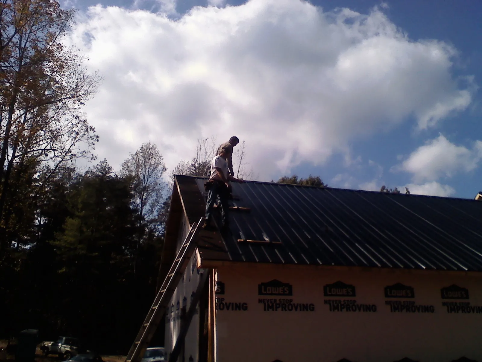 Roofer fastening dark metal panels high against a cloudy sky, from a Roof Inspection job in Mineral Point